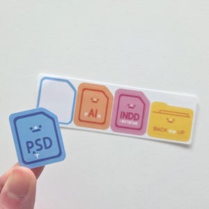 May include: A light blue sticker with the letters "PSD" and a small upward arrow. A hand holds the sticker in front of a white background with a strip of stickers. The strip has file-shaped stickers with the words "PAIN", "INDD -ecisive", and "BACK me UP".