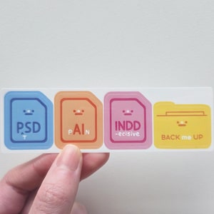 K&ouml;nnte beinhalten: Ein rechteckiger Aufkleber mit vier farbigen Dateisymbolen. Die Symbole sind blau, orange, rosa und gelb, jedes mit einem l&auml;chelnden Gesicht und Text: "PSD", "PAIN", "INDD -ecisive" und "BACK me UP".