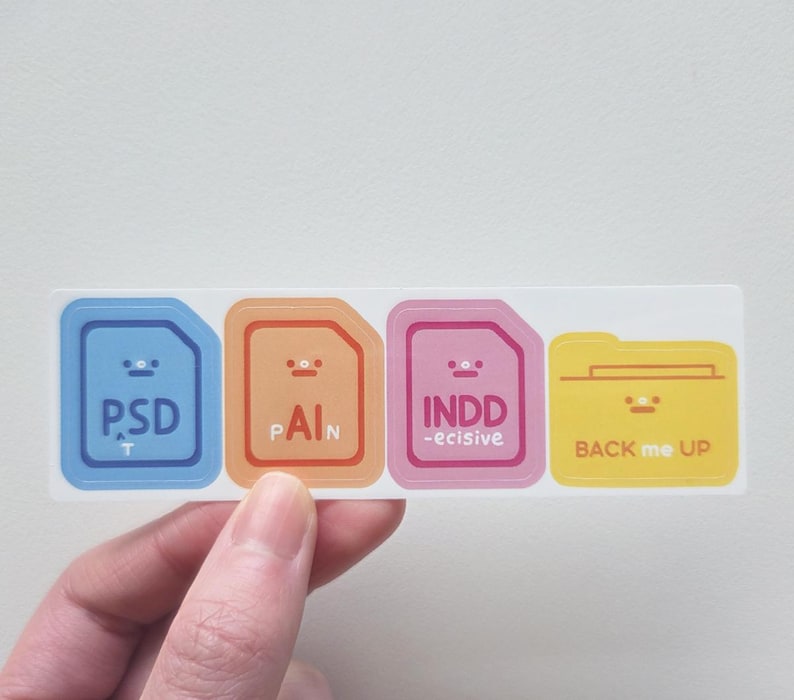 K&ouml;nnte beinhalten: Ein rechteckiger Aufkleber mit vier farbigen Dateisymbolen. Die Symbole sind blau, orange, rosa und gelb, jedes mit einem l&auml;chelnden Gesicht und Text: "PSD", "PAIN", "INDD -ecisive" und "BACK me UP".