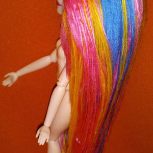 May include: A doll with long, colorful hair. The hair is pink, yellow, blue, and orange. The doll is nude and has a simple face.