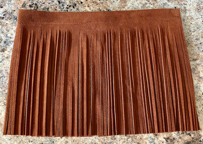 May include: A brown suede fringe trim with a straight edge. The fringe is about 2 inches long.