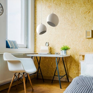 May include: A modern home office setup featuring a white desk with black legs, a white chair with wooden legs, and two white spherical pendant lights. A wall clock, books, and decorative items complete the scene. The background has a light wood paneling.