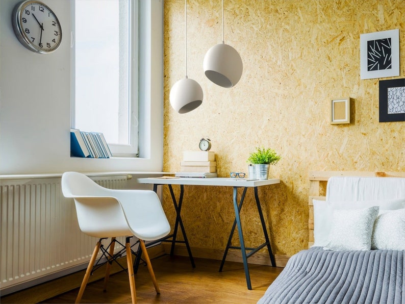 May include: A modern home office setup featuring a white desk with black legs, a white chair with wooden legs, and two white spherical pendant lights. A wall clock, books, and decorative items complete the scene. The background has a light wood paneling.