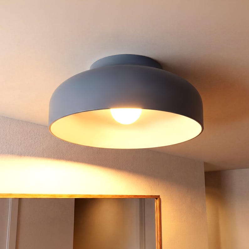 A smokey blue ceiling light fixture with a rounded shade and a bright light bulb installed in a modern hallway. The interior of the shade is a white clay . The fixture is mounted on a white ceiling next to decorative mirror. the room glows in warm light of the fixutue