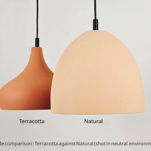 May include: Two pendant lights, one terracotta and one natural, hang from black cords. The terracotta light has a teardrop shape, while the natural light is a rounded dome. The text below reads "Terracotta" and "Natural".