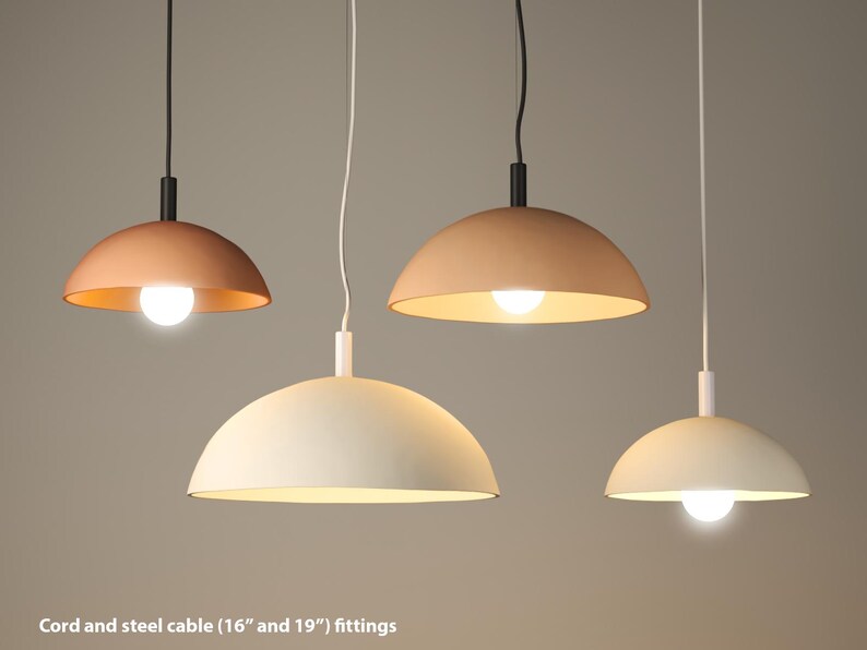 May include: Four pendant lights with a dome shape in shades of beige and copper. Each light has a visible bulb and hangs from a cord and steel cable. The fittings are 16 and 19 inches.