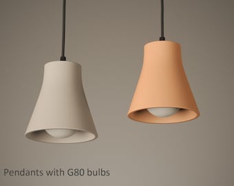 May include: Two pendant lights with G80 bulbs hanging from black cords. One shade is a light beige colour and the other is a soft terracotta orange. Both fixtures feature a smooth, flared bell-shaped design. The text Pendants with G80 bulbs is visible.