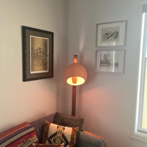 May include: A floor lamp with a spherical, matte peach-colored shade and a wooden stand, positioned next to a gray sofa adorned with a multi-colored striped throw blanket and two patterned accent pillows featuring geometric designs.