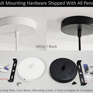 May include: White and black ceiling mount hardware for pendants. Includes a 5-inch mounting plate, cross beam, mounting screws, cord grips, and insulation caps. The image shows the hardware in both white and black, with the text "Default Mounting Hardware Shipped With All Pendants."