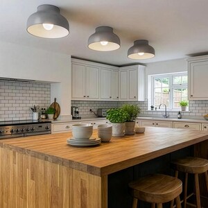A modern kitchen with a large wooden island and three gray ceiling lights. White cabinets and a white brick backsplash complement the island. Two wooden stools are placed near the island.