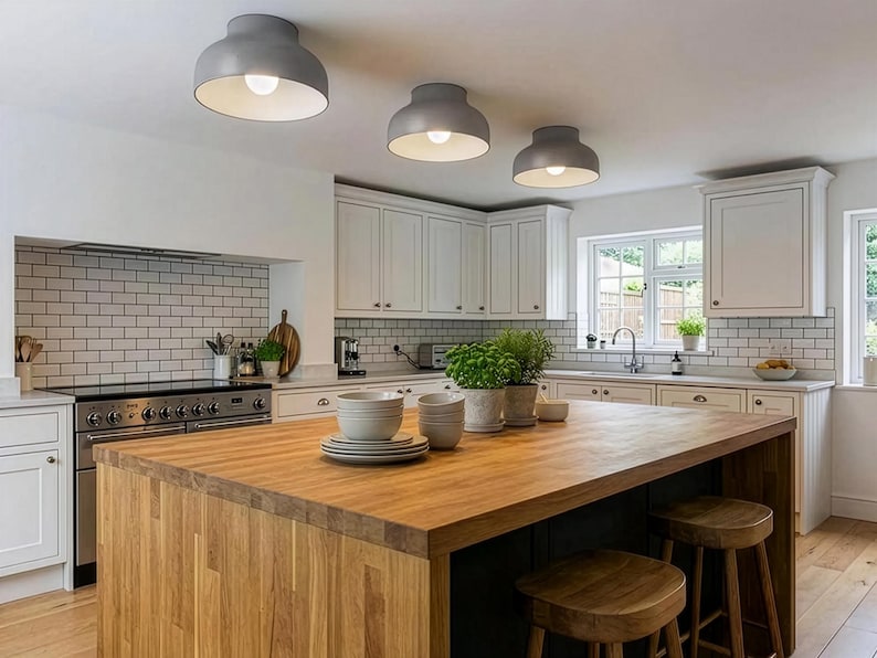 A modern kitchen with a large wooden island and three gray ceiling lights. White cabinets and a white brick backsplash complement the island. Two wooden stools are placed near the island.