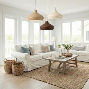 May include: Three pendant lights with smooth, bell-shaped shades in tan, cream, and dark brown, suspended from the ceiling. These fixtures feature a matte finish and hang at varying heights above a living room seating area with white sofas.