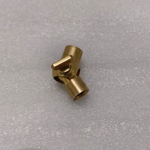 Könnte beinhalten: Ein Messing-Drehgelenk mit Hebel. Das Fitting hat eine zylindrische Form mit einem Drehgelenk und einem kleinen Hebel zur Einstellung. Das Metall hat ein poliertes, goldenes Aussehen. Der Artikel wird wahrscheinlich in Sanitär- oder mechanischen Anwendungen verwendet.