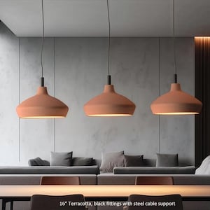 May include: Three terracotta-colored pendant lights with black fittings and steel cable support. The lamps are suspended above a dining table and a gray sofa. The lamps are approximately 16 inches in diameter.