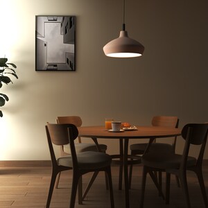 May include: A round wooden dining table with four matching chairs featuring upholstered seats. A pendant light hangs above the table, which holds a glass of orange juice and a small plate. A potted plant stands to the left, and a framed print hangs on the wall.