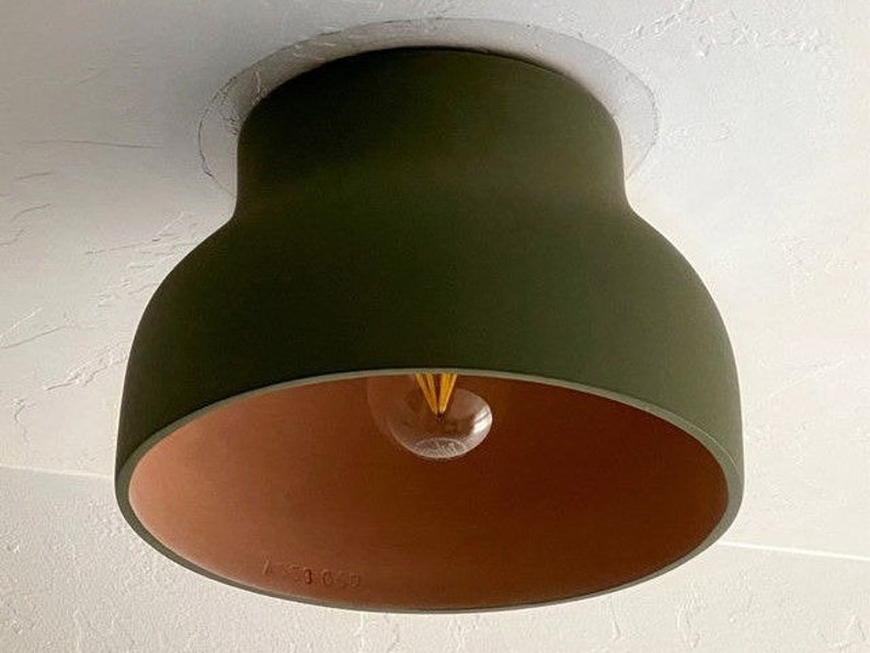Olive green ceiling light fixture with a terracotta-colored interior. The light has a rounded, bell-like shape and a visible lightbulb. The fixture is mounted on a white ceiling.