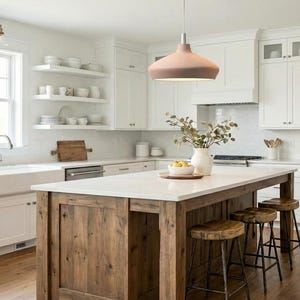 May include: A kitchen featuring white cabinetry, a farmhouse sink, and a large wooden island with a white countertop. Three wooden stools with metal legs are tucked under the island. A matte pink pendant light hangs above the island.