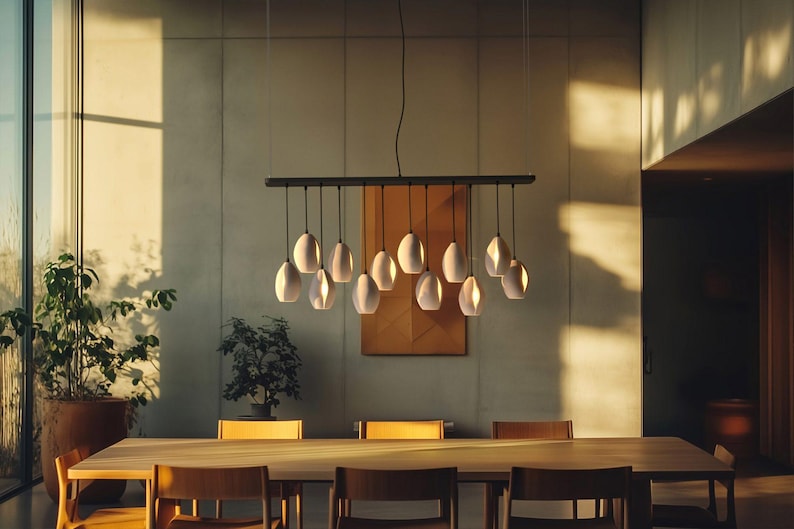 May include: A modern dining room featuring a long wooden table with several chairs. Above the table hangs a black light fixture with multiple white, egg-shaped pendant lights. The room has large windows and a neutral color palette.