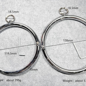 Könnte beinhalten: Zwei silberne Metallkragen mit einem Durchmesser von 118,5 mm und 138 mm. Die Kragen sind 10 mm breit und haben einen kleinen Ring oben. Die Kragen wiegen etwa 290 Gramm und 330 Gramm.