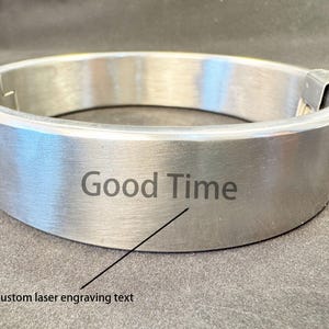 May include: A brushed silver-tone metal collar featuring a smooth, circular band design. The front surface is engraved with the text "Good Time" and includes a small arrow pointing to the phrase with the label "Custom laser engraving text".