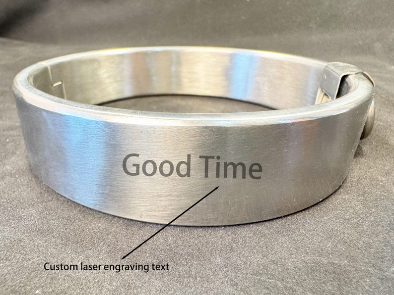 May include: A brushed silver-tone metal collar featuring a smooth, circular band design. The front surface is engraved with the text "Good Time" and includes a small arrow pointing to the phrase with the label "Custom laser engraving text".