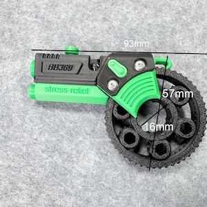 Può includere: Un giocattolo antistress verde e nero. Il giocattolo è lungo 93 mm, con un ingranaggio circolare di 57 mm di diametro e 16 mm di spessore. Il testo "BB369" e "stress-relief" sono stampati sul giocattolo.