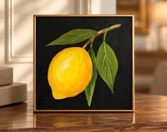 Puede incluir: Un cuadro cuadrado enmarcado que muestra un limón amarillo brillante con tres hojas verdes unidas a un tallo, sobre un fondo negro sólido. La obra de arte está encerrada en un marco fino de metal dorado con un acabado liso.
