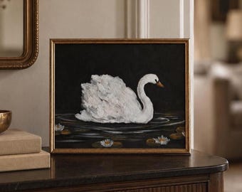 May include: A rectangular framed painting featuring a white swan swimming on dark water. The swan has textured brushstrokes and an orange beak. Several white water lilies with yellow centres float on the water surface against a black background.