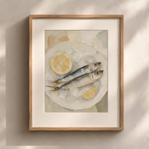 May include: A framed painting of two sardines on a white plate with a lemon slice. The artwork has a textured, oil-paint style, with a neutral color palette of white, yellow, and blue. The frame is a light brown color.