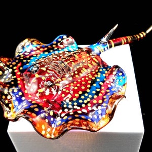 May include: A glass sculpture of a stingray with a red, blue and yellow spotted pattern. The stingray is made of clear glass with a brown tail.