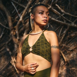 Peut inclure: Haut de bikini vert olive et short assorti. Le haut présente un motif géométrique noir et un anneau circulaire. Le short a une taille haute et des détails lacés sur les côtés. L'ensemble est en tissu doux et extensible.