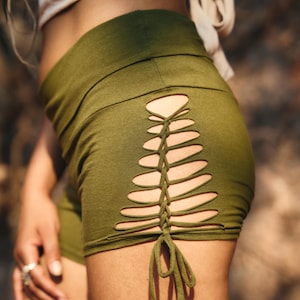Peut inclure: Shorts vert olive avec un design découpé unique sur le côté. Les shorts présentent une série de fentes horizontales lacées avec un lien en tissu assorti. Les shorts sont faits d'une matière douce et extensible.