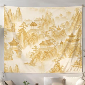 May include: A large, rectangular tapestry featuring a golden-toned Asian landscape with pagodas, mountains, and trees. The artwork is displayed on a white wall above a modern living room setting with neutral-toned furniture and decor.
