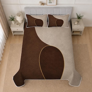Peut inclure: Un ensemble de literie comprenant une courtepointe et deux taies d'oreiller avec un design bicolore en brun foncé et beige. La parure présente de grandes formes abstraites incurvées soulignées par un fin passepoil doré sur le lit.