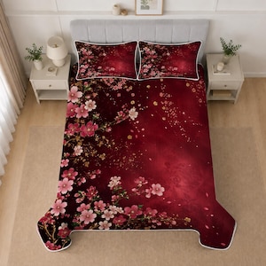 Può includere: Un set di biancheria da letto con uno sfondo rosso intenso e un motivo stampato di fiori di ciliegio rosa con accenti dorati sparsi. Il set include un grande piumino e due cuscini rettangolari abbinati, tutti rifiniti con un bordo bianco.