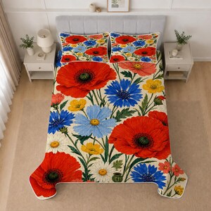 May include: A bed quilt featuring a botanical print of large red poppies, blue cornflowers, yellow buttercups, and white daisies on a cream background. The matching pillow shams display the same floral pattern with vibrant red and blue flowers.