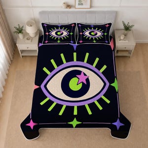 May include: A black bedspread and two matching pillowcases featuring a large central eye graphic with a lime green pupil, a light purple iris, and a pink star accent. The design includes bright neon green eyelashes and colorful four-pointed stars.
