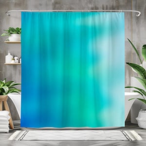 Op de afbeelding: Een douchegordijn met een wazig, abstract ontwerp. Het gordijn heeft verticale strepen in blauw en teal, waardoor een gradiënteffect ontstaat. Het ontwerp doet denken aan water of een aquarel, wat een kalmerende esthetiek aan een badkamer toevoegt.