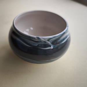 May include: A small, round ceramic bowl with a dark blue and white marbled design. The interior is a light cream colour. The bowl has a wide opening and a smooth, glossy finish. This decorative bowl is suitable for holding small items.