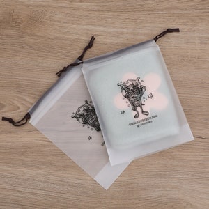 May include: Two clear plastic drawstring bags with a black and white cartoon illustration of a dog wearing a space helmet. The text on the bag reads "www.puppytees.com @puppytees".