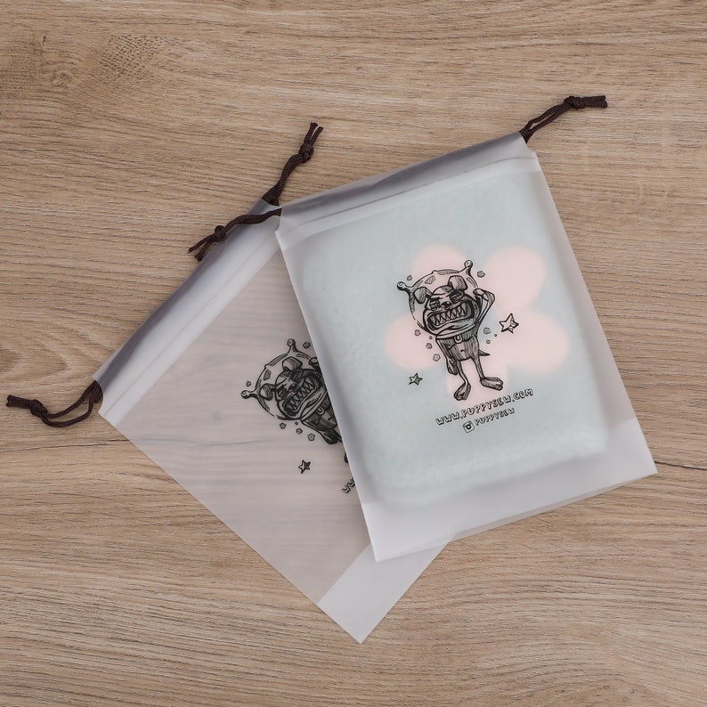 May include: Two clear plastic drawstring bags with a black and white cartoon illustration of a dog wearing a space helmet. The text on the bag reads "www.puppytees.com @puppytees".