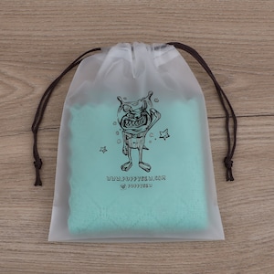 May include: A clear plastic drawstring bag with a teal blue fabric lining. The bag features a black and white illustration of a cartoon monster with stars and the text "www.puppysew.com @puppysew".