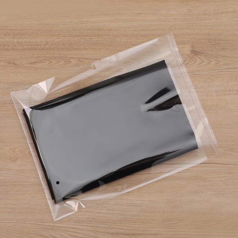 May include: A black item is sealed within a transparent plastic bag. The bag's clarity reveals the dark color of the contents. The packaging rests on a light brown wooden surface.