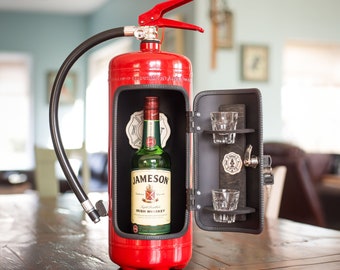 Può includere: Un estintore rosso con una maniglia nera e una piccola porta che si apre per rivelare una bottiglia di Jameson Irish Whiskey e due bicchieri da shot.