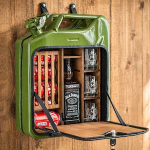 May include: A green metal jerry can converted into a bar cabinet. It contains a wooden rack for cans, a bottle of Jack Daniel's whiskey, three glasses, and a small bottle. The cabinet door is open, displaying the contents within.