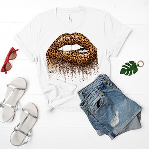 May include: White t-shirt with a leopard print lip design. The lip is outlined in black and has a glitter effect. The shirt is paired with denim shorts.