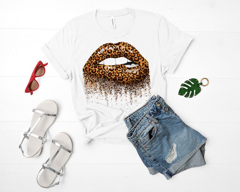 May include: White t-shirt with a leopard print lip design. The lip is outlined in black and has a glitter effect. The shirt is paired with denim shorts.