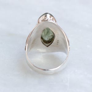 K&ouml;nnte beinhalten: Ein silberner Ring mit einem gr&uuml;nen Edelstein, der in einer Marquise-Form gefasst ist. Der Ring hat ein detailliertes Design an der Band.