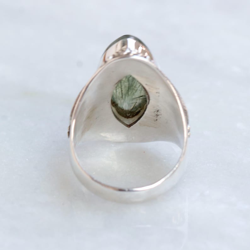 K&ouml;nnte beinhalten: Ein silberner Ring mit einem gr&uuml;nen Edelstein, der in einer Marquise-Form gefasst ist. Der Ring hat ein detailliertes Design an der Band.