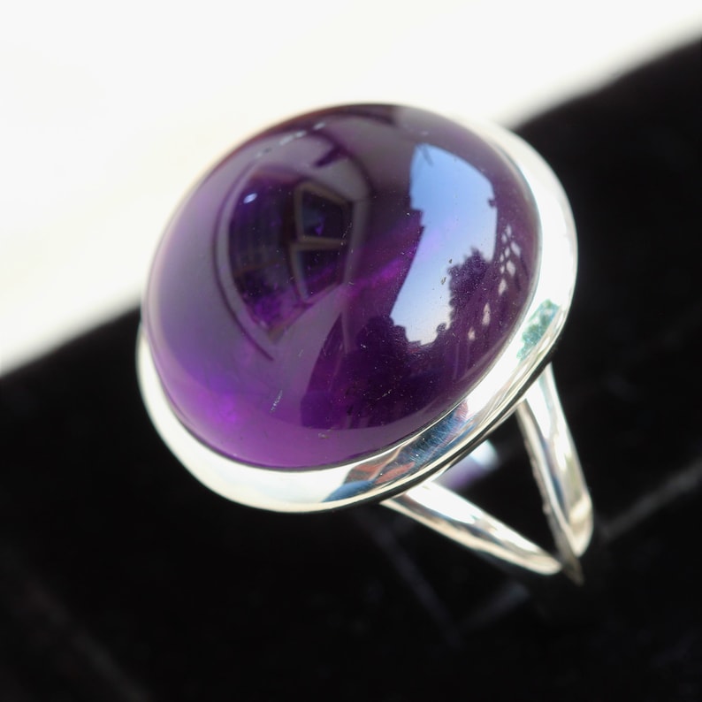 May include: A silver ring with a large, round, purple amethyst gemstone.